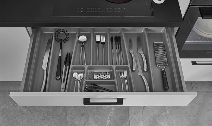 Wir sehen eine geöffnete Besteckschublade. Dei Front ist grau und der Griff ist schwarz. Wir sehen eine geöffnete Besteckschublade. Dei Front ist grau und der Griff ist schwarz.