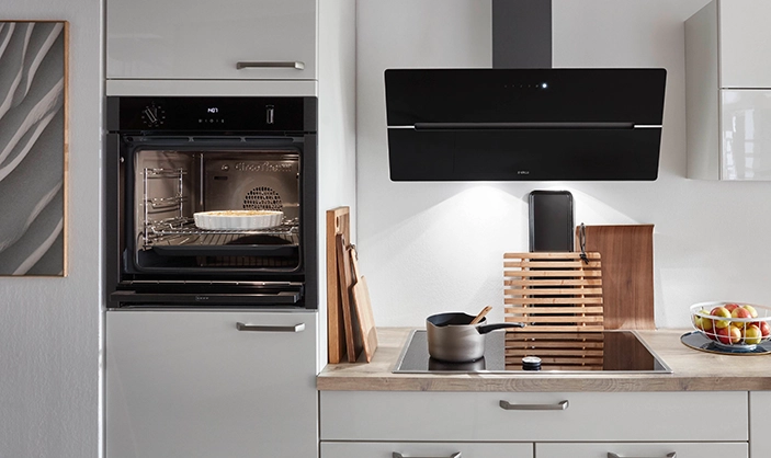 Wir sehen den Ausschnitt einer gut ausgestatteten hellen Pantryküche mit schwarzer Dunsthaube und eingebautem Backofen. Wir sehen den Ausschnitt einer gut ausgestatteten hellen Pantryküche mit schwarzer Dunsthaube und eingebautem Backofen.