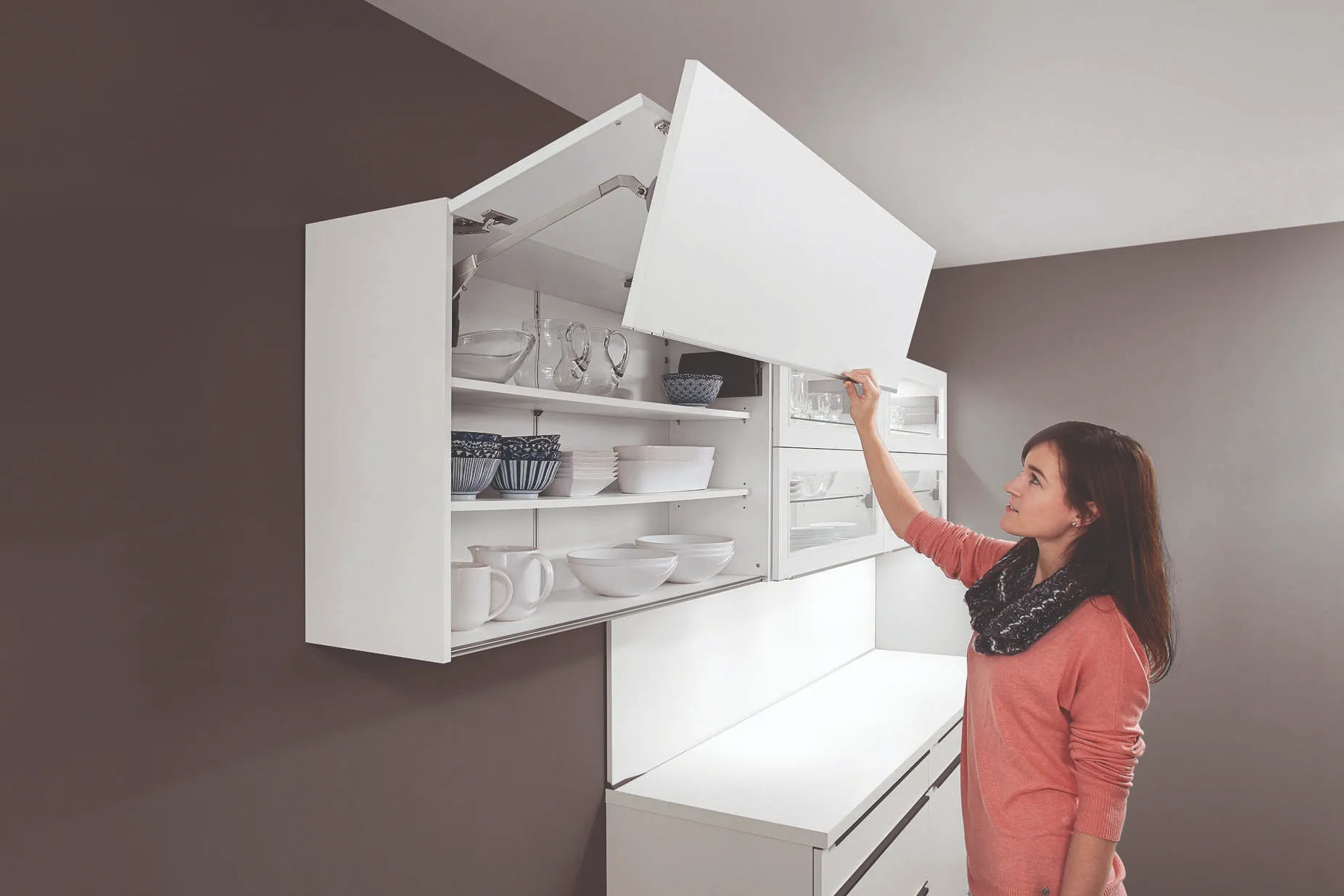 Junge Frau öffnet einen Wandschrank mit Falttür als platzsparende Lösung in der Singleküche Junge Frau öffnet einen Wandschrank mit Falttür als platzsparende Lösung in der Singleküche