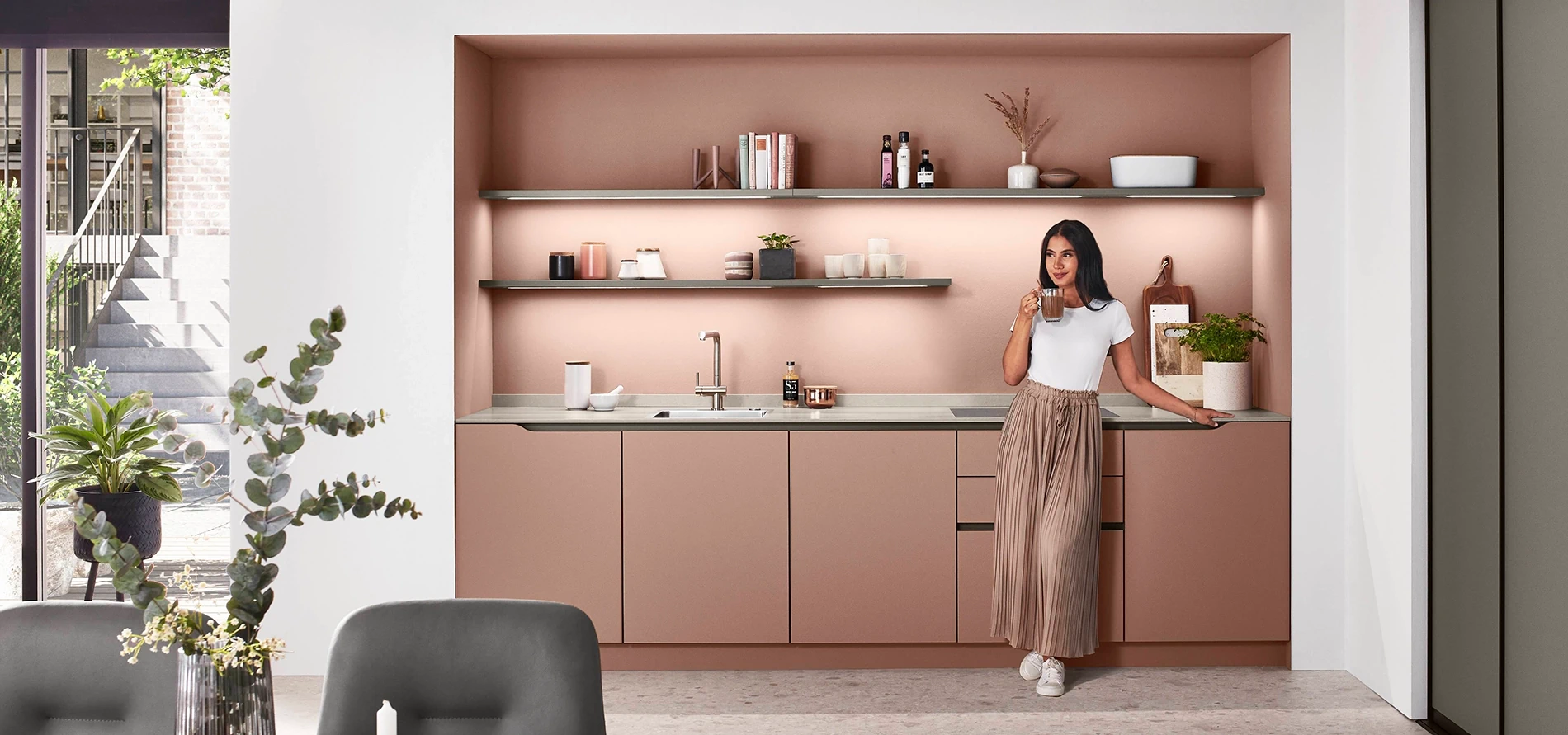 Junge Frau in einer modernen rosa Singleküche in kompakter Küchenzeile Junge Frau in einer modernen rosa Singleküche in kompakter Küchenzeile