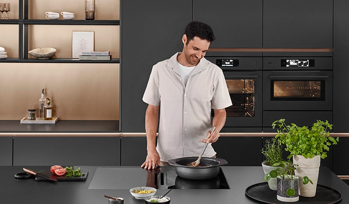 Mann bereitet Essen in einer modernen schwarzen Singleküche zu Mann bereitet Essen in einer modernen schwarzen Singleküche zu