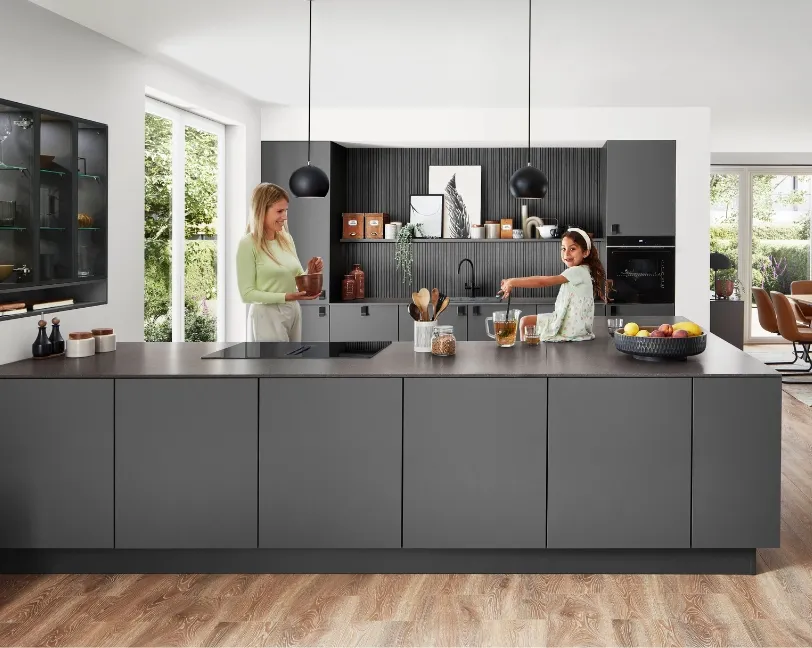 Moderne smarte Küche mit schwarzer Kücheninsel, an der eine Frau gemeinsam mit einem Kind Speisen zubereitet. Moderne smarte Küche mit schwarzer Kücheninsel, an der eine Frau gemeinsam mit einem Kind Speisen zubereitet.