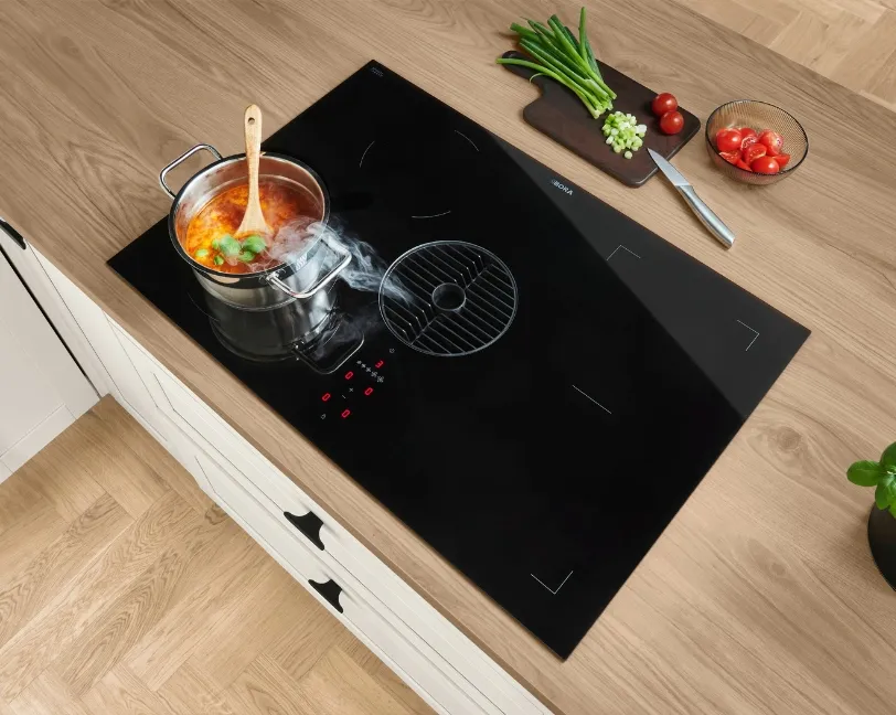 Smarte Küche mit schwarzem Induktionskochfeld und integriertem Dunstabzug beim Kochen mit einem Topf und frischen Zutaten. Smarte Küche mit schwarzem Induktionskochfeld und integriertem Dunstabzug beim Kochen mit einem Topf und frischen Zutaten.