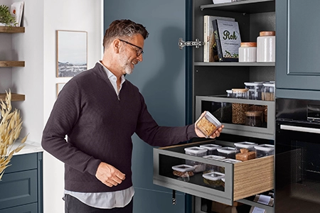 Ein Mann in dunklem Paull entnimmt einem Hochschrank eine Dose. Der Innenschubkasten befindet sich auf einer ergonomisch angenehmen Höhe. Ein Mann in dunklem Paull entnimmt einem Hochschrank eine Dose. Der Innenschubkasten befindet sich auf einer ergonomisch angenehmen Höhe.