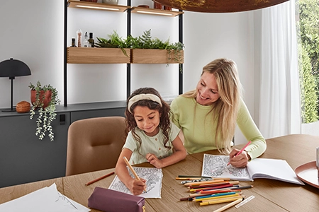 Mutter und Tochter malen am Küchentisch. Auf dem Tisch liegen Malbücher und Buntstifte. Die Mutter trägt ein hellgrünes Shirt, das Mädchen auch, dazu hat es einen hellen Stoffhaarreif. Mutter und Tochter malen am Küchentisch. Auf dem Tisch liegen Malbücher und Buntstifte. Die Mutter trägt ein hellgrünes Shirt, das Mädchen auch, dazu hat es einen hellen Stoffhaarreif.