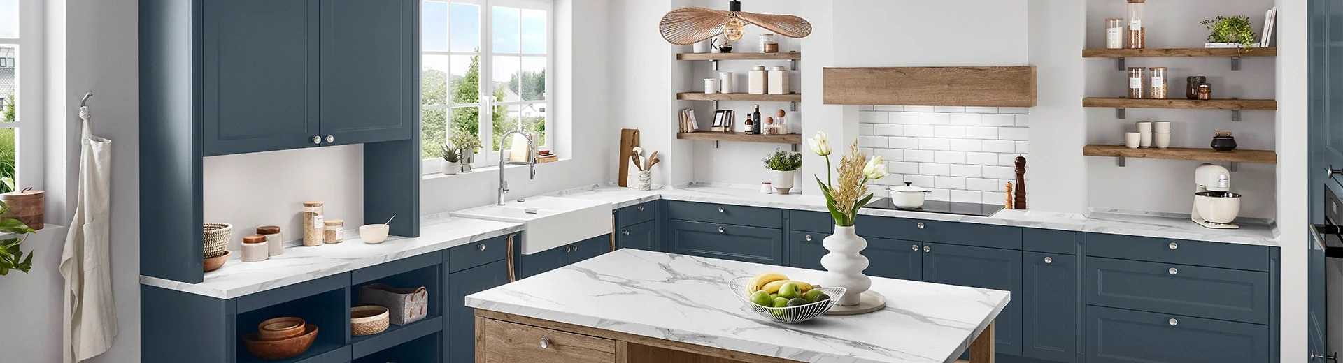 Ausschnitt einer Küche im Landhausstil mit dunkelblauen Fronten und weißer Arbeitsplatte. In der Mitte steht eine Kochinsel. Ausschnitt einer Küche im Landhausstil mit dunkelblauen Fronten und weißer Arbeitsplatte. In der Mitte steht eine Kochinsel.