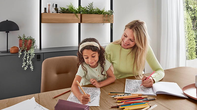 Mutter und Tochter sitzen am Küchentisch, beide malen etwas aus. Mutter und Tochter sitzen am Küchentisch, beide malen etwas aus.
