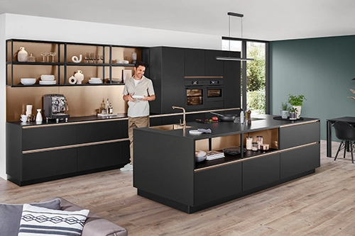 Moderne schwarze Küche mit Kochinsel, offenen Regalen und einer Person im Raum. Moderne schwarze Küche mit Kochinsel, offenen Regalen und einer Person im Raum.