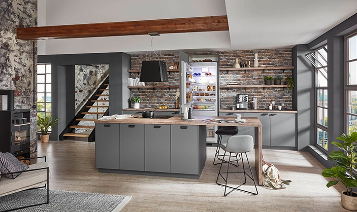 Industrial-Style Insel-Küche mit grauen Fronten, Holzarbeitsplatte und offenen Regalen vor Ziegelwand. Industrial-Style Insel-Küche mit grauen Fronten, Holzarbeitsplatte und offenen Regalen vor Ziegelwand.