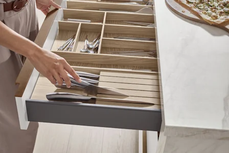Geöffnete Küchenschublade mit Besteckeinsatz aus Holz, Hand legt Messer hinein, organisiert und funktional für moderne Küchenaufbewahrung. Geöffnete Küchenschublade mit Besteckeinsatz aus Holz, Hand legt Messer hinein, organisiert und funktional für moderne Küchenaufbewahrung.