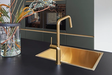 Ausschnitt einer Küche, bei der die Spüle ein wichtiger Faktor in Bezug auf das Budget ist. Die Spüle ist goldfarben und in eine schwarze Arbeitsplatte eingelasssen. Ausschnitt einer Küche, bei der die Spüle ein wichtiger Faktor in Bezug auf das Budget ist. Die Spüle ist goldfarben und in eine schwarze Arbeitsplatte eingelasssen.