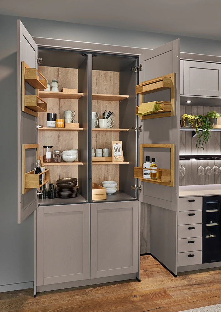 Ein geöffneter Küchenfrühstückschrank mit hellbraunen Rahmenfronten. Im Innern sehen wir Besteck und Küchenutensilien. Ein geöffneter Küchenfrühstückschrank mit hellbraunen Rahmenfronten. Im Innern sehen wir Besteck und Küchenutensilien.