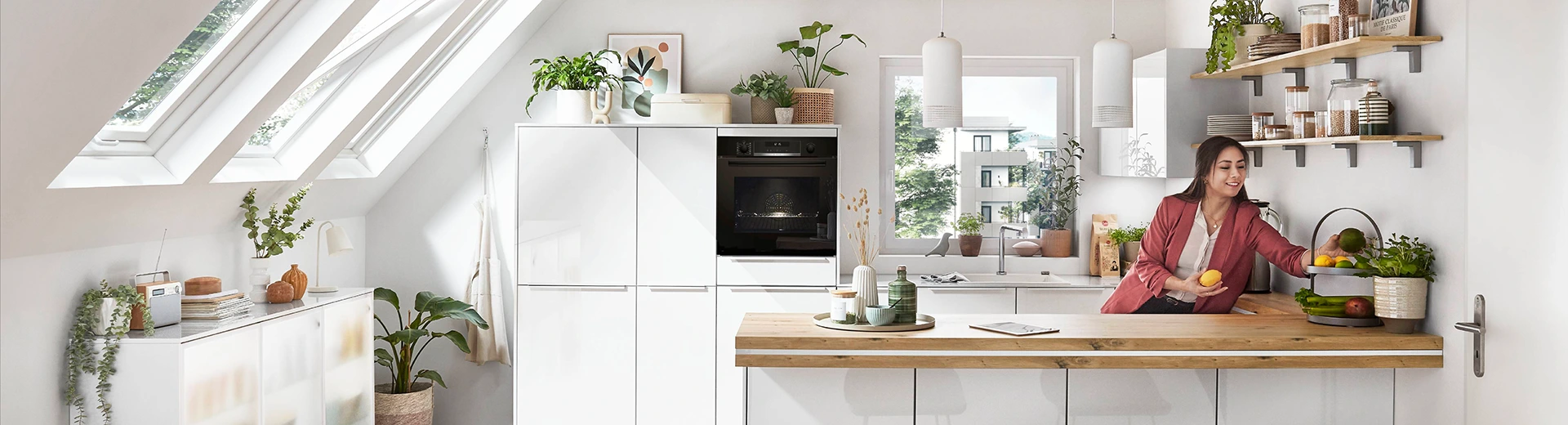 Junge Frau mit rotem Blazer in einer lichtdurchfluteten weißen grifflosen Küche mit Zeile und Insel. Junge Frau mit rotem Blazer in einer lichtdurchfluteten weißen grifflosen Küche mit Zeile und Insel.