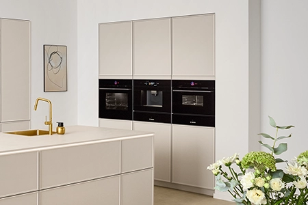 Backofen, Dampfgarer in einer Hochschrankzeile in einer sandfarbenen Küche mit Rahmenfronten. Im Vordergrund eine Insel mit Spüle Backofen, Dampfgarer in einer Hochschrankzeile in einer sandfarbenen Küche mit Rahmenfronten. Im Vordergrund eine Insel mit Spüle