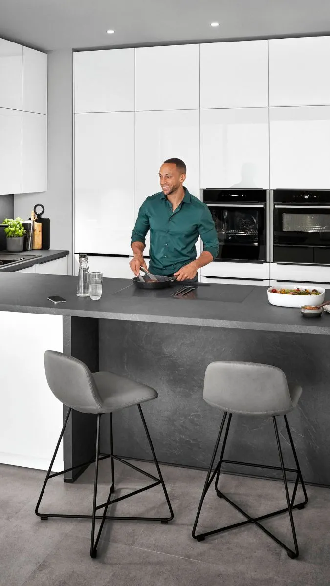 Moderne Küche mit weiß-hochglänzenden Fronten, dunkler Arbeitsplatte und zwei Barhockern an einer Kochinsel. Moderne Küche mit weiß-hochglänzenden Fronten, dunkler Arbeitsplatte und zwei Barhockern an einer Kochinsel.