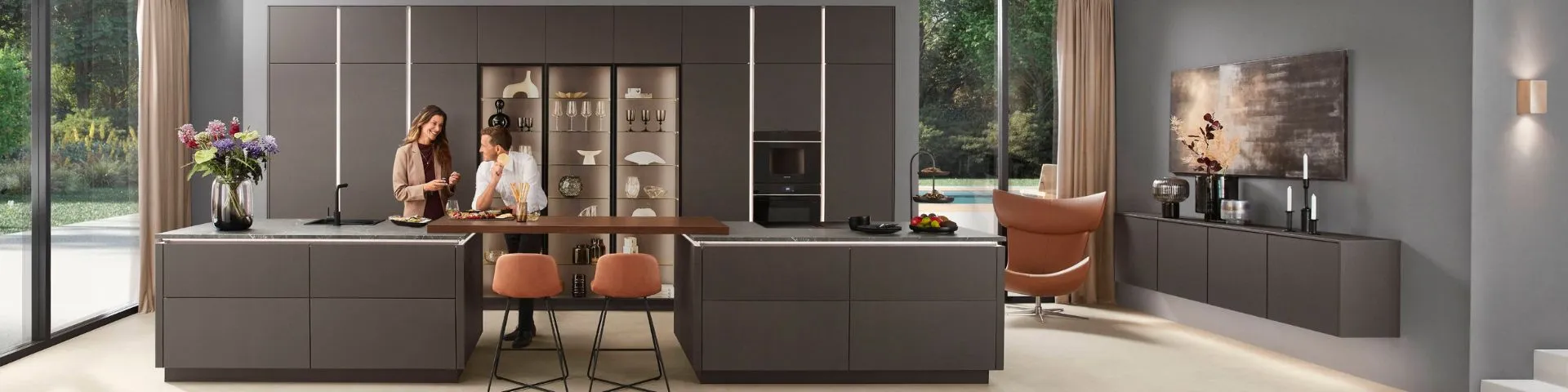 Elegante, dunkel gehaltene Designküche mit zwei Inseln, Glasvitrinen und bodentiefen Fenstern mit Blick ins Grüne. Elegante, dunkel gehaltene Designküche mit zwei Inseln, Glasvitrinen und bodentiefen Fenstern mit Blick ins Grüne.