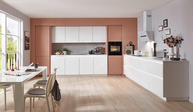 Zweizeilige Küche mit glatten, weiß matten, grifflosen Fronten. Links steht ein Esstisch mit Stühlen. Zweizeilige Küche mit glatten, weiß matten, grifflosen Fronten. Links steht ein Esstisch mit Stühlen.