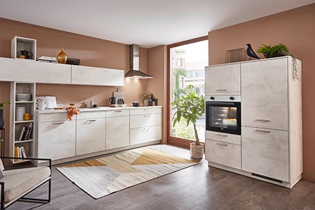 Betonweiße zweizeilige Küche mit zwei Highboards sowie einer Zeile aus vier Unterschränken und 2 Wandklappenschränken. Die Griffe sind grau. Links sehen wir die Sitzfläche eines Stuhls. Betonweiße zweizeilige Küche mit zwei Highboards sowie einer Zeile aus vier Unterschränken und 2 Wandklappenschränken. Die Griffe sind grau. Links sehen wir die Sitzfläche eines Stuhls.